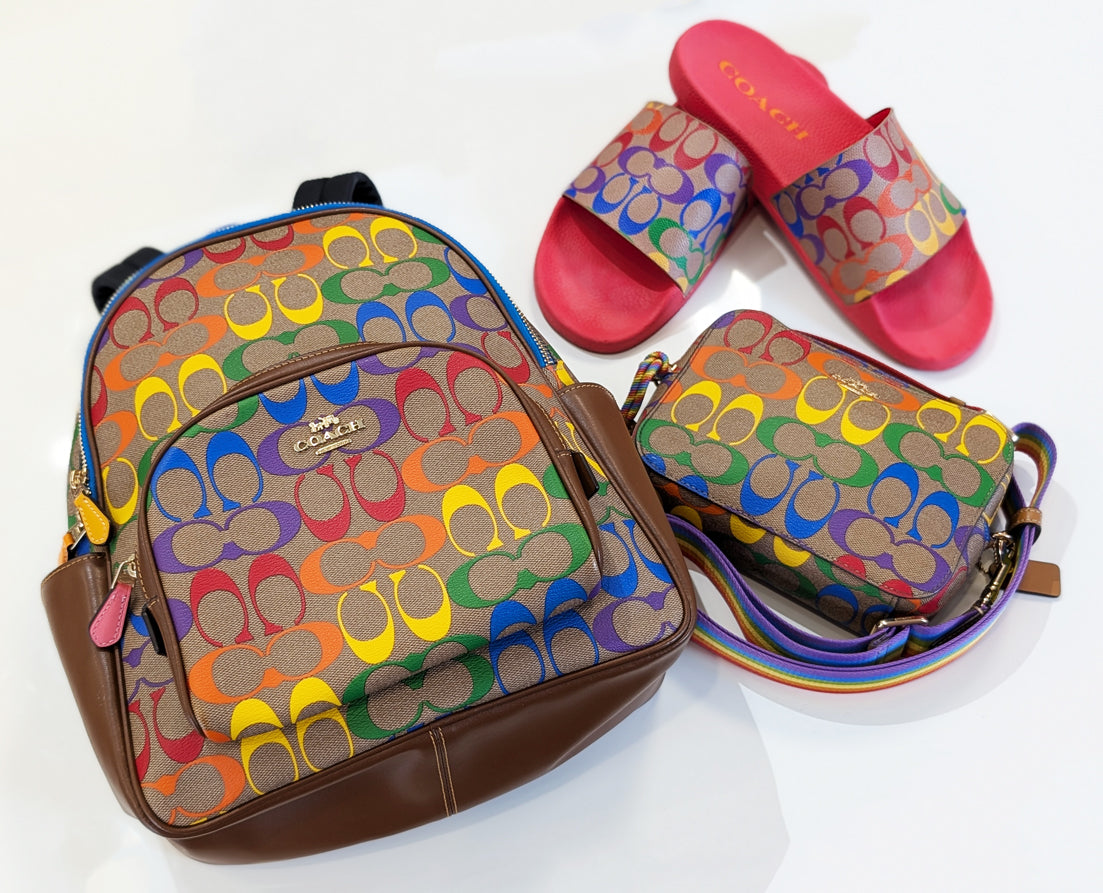 A signature rainbow print backpack, slide sandals, and crossbody from Coach's 2021 Pride collection on a white background.