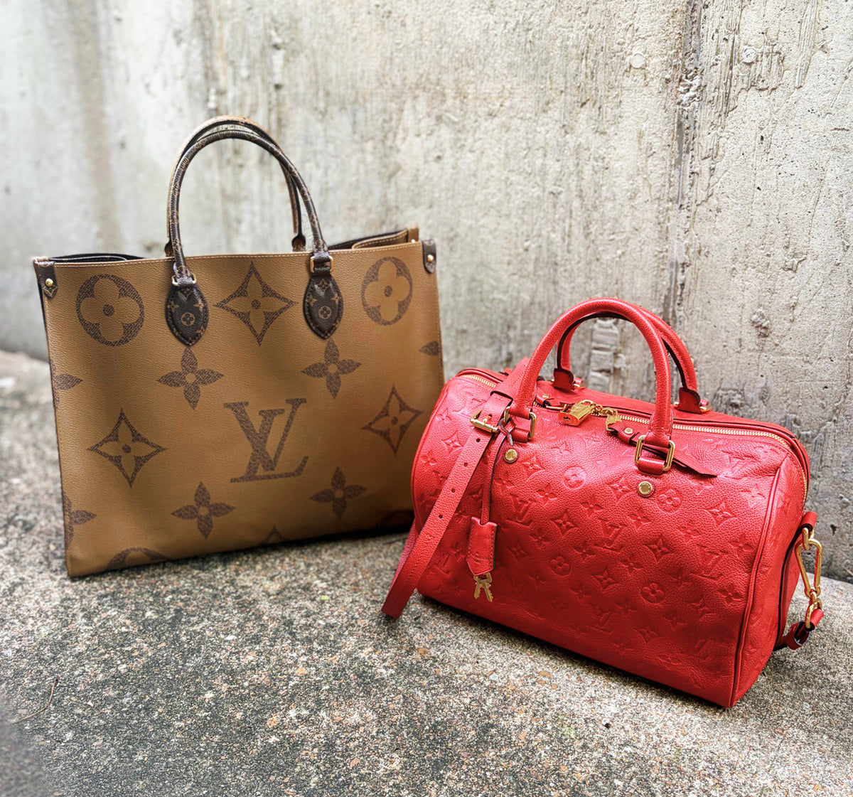 Two Louis Vuitton handbags in front of a concrete background.