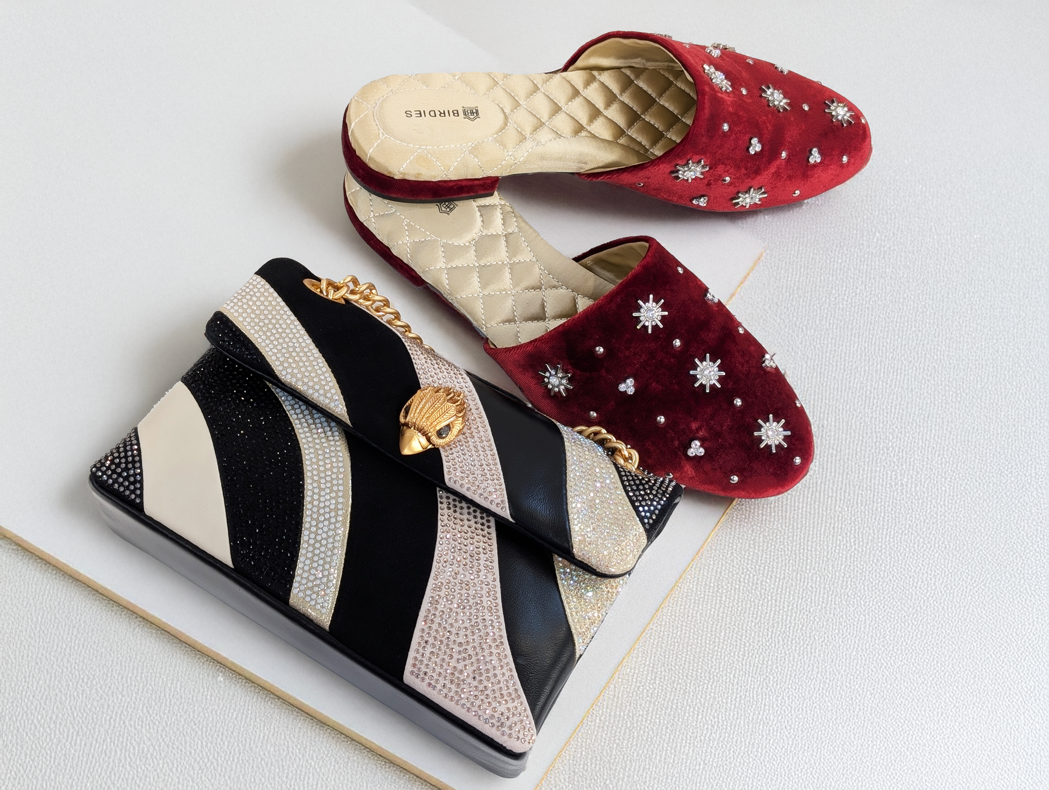 A photo of a pair of red, crystal embellished slides and a black and white glitter handbag.