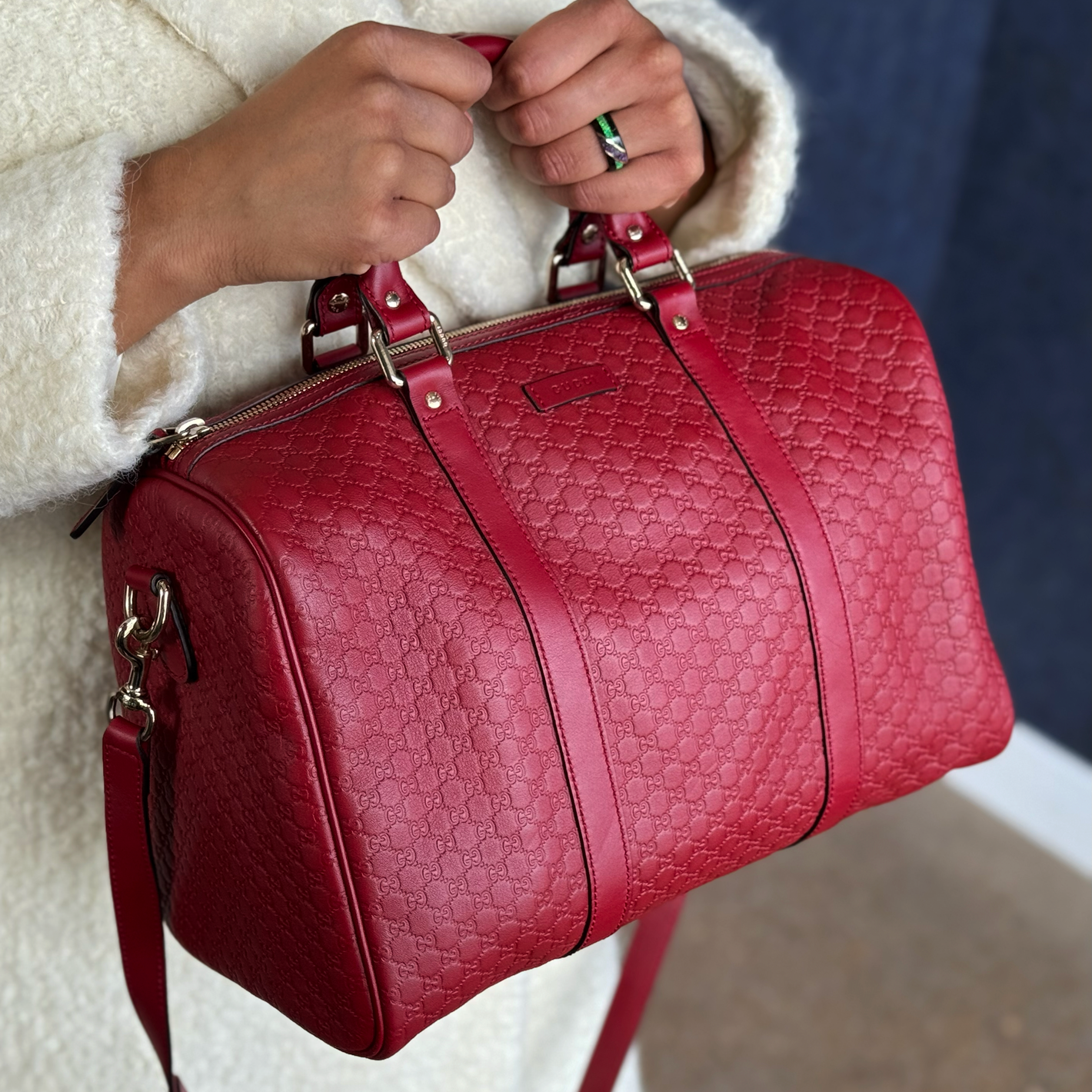 A woman wearing a cream shearling coat, holding a red Gucci Boston Joy handbag.