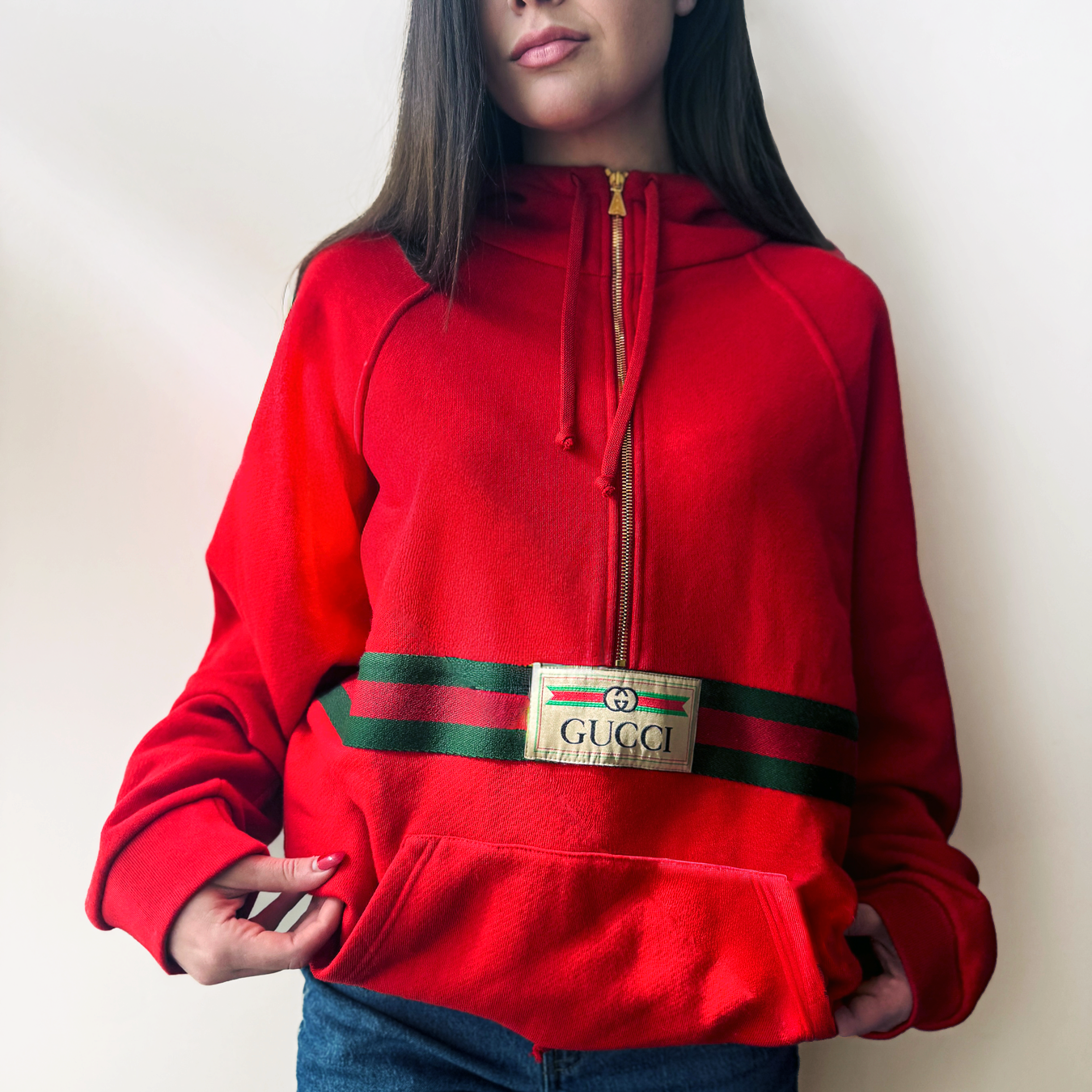 A woman wearing a red Gucci hoodie against an off-white background.