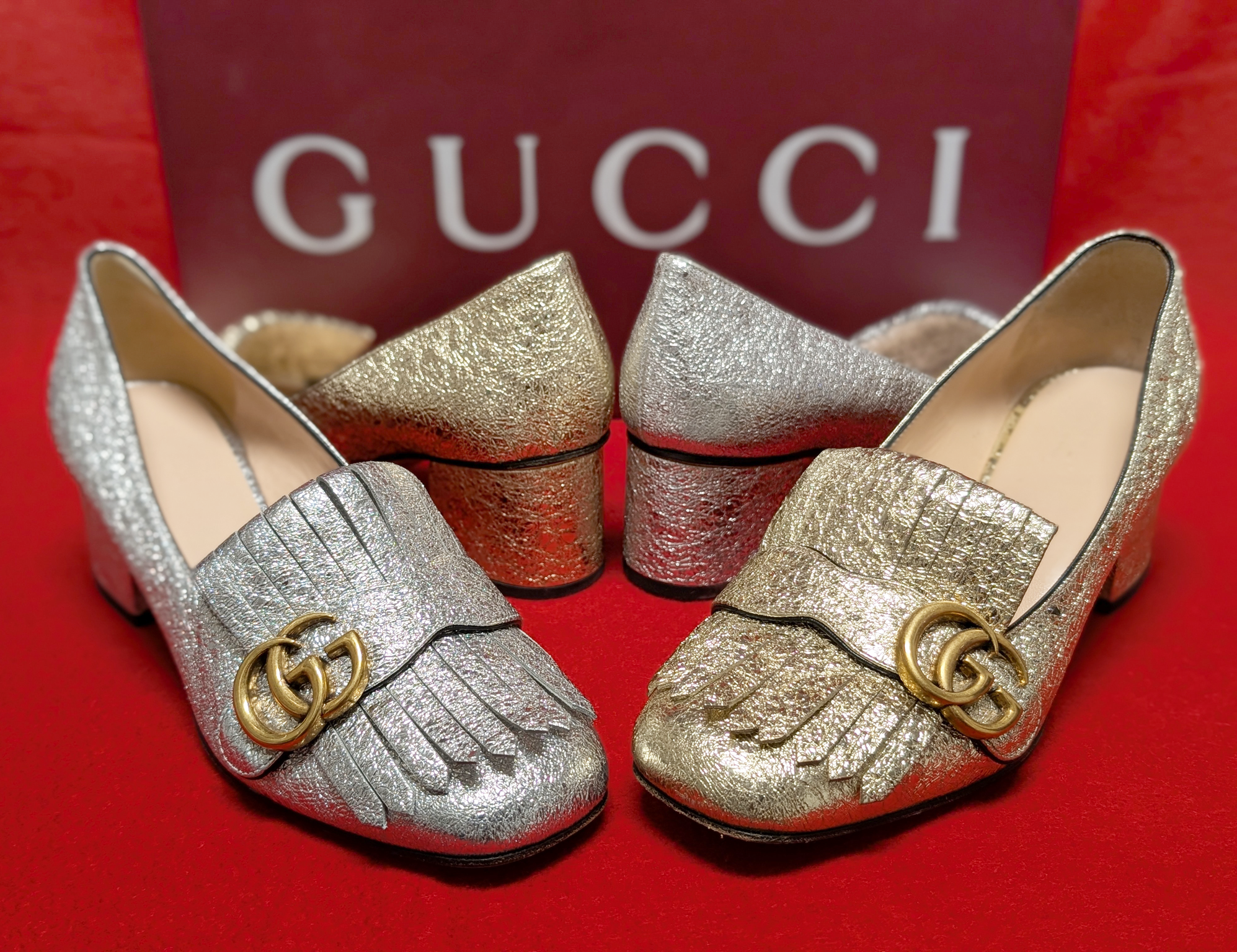 A pair of gold and silver glitter Gucci heels on a red background.