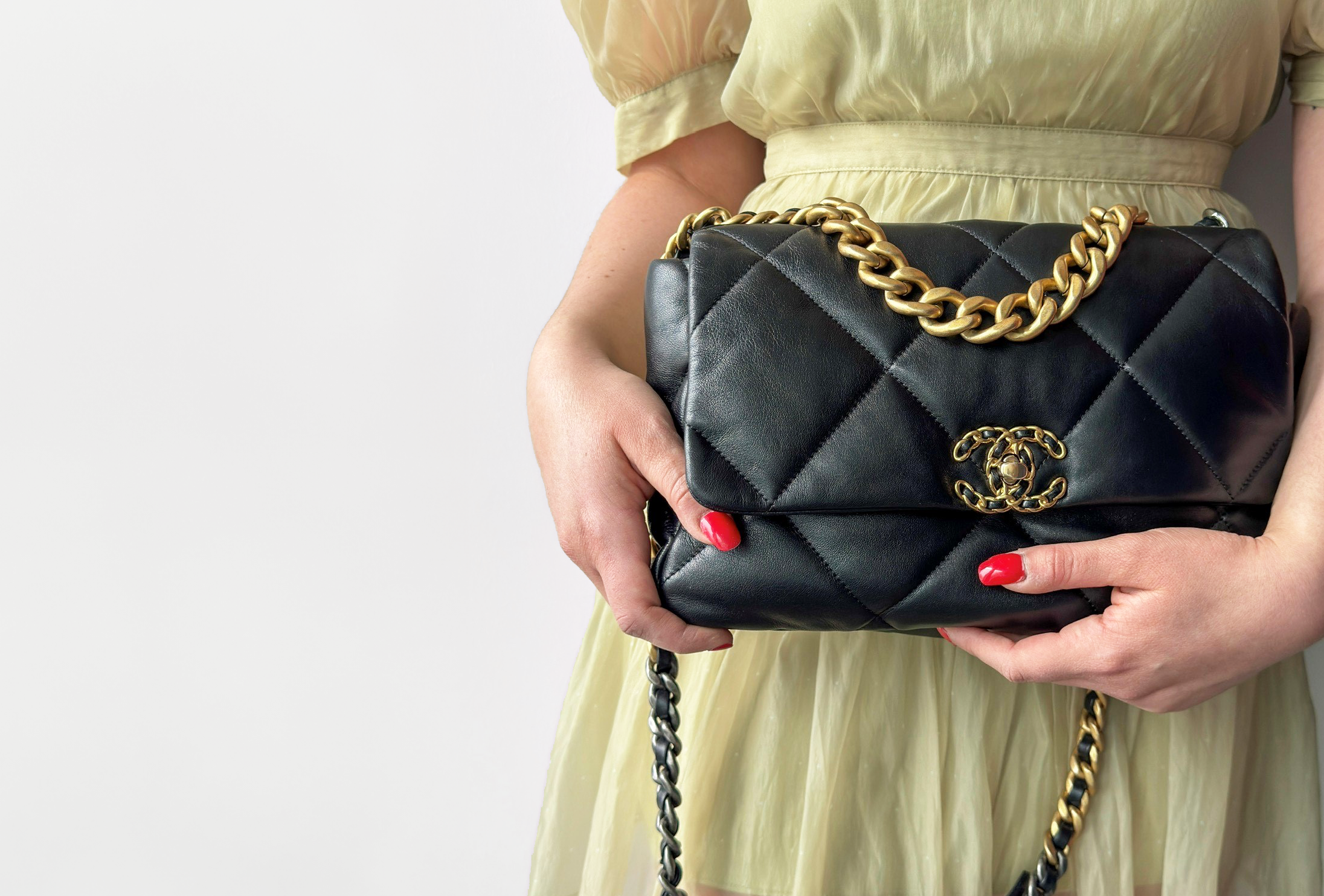 A picture of a woman with red fingernails and a green dress, holding a Chanel Flap bag.