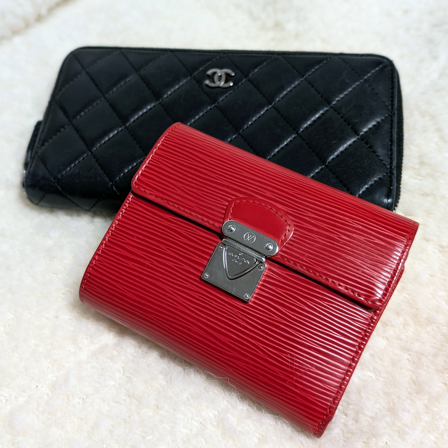 Black quilted Chanel wallet and red Epi Leather Louis Vuitton wallet on a shearling cream background.