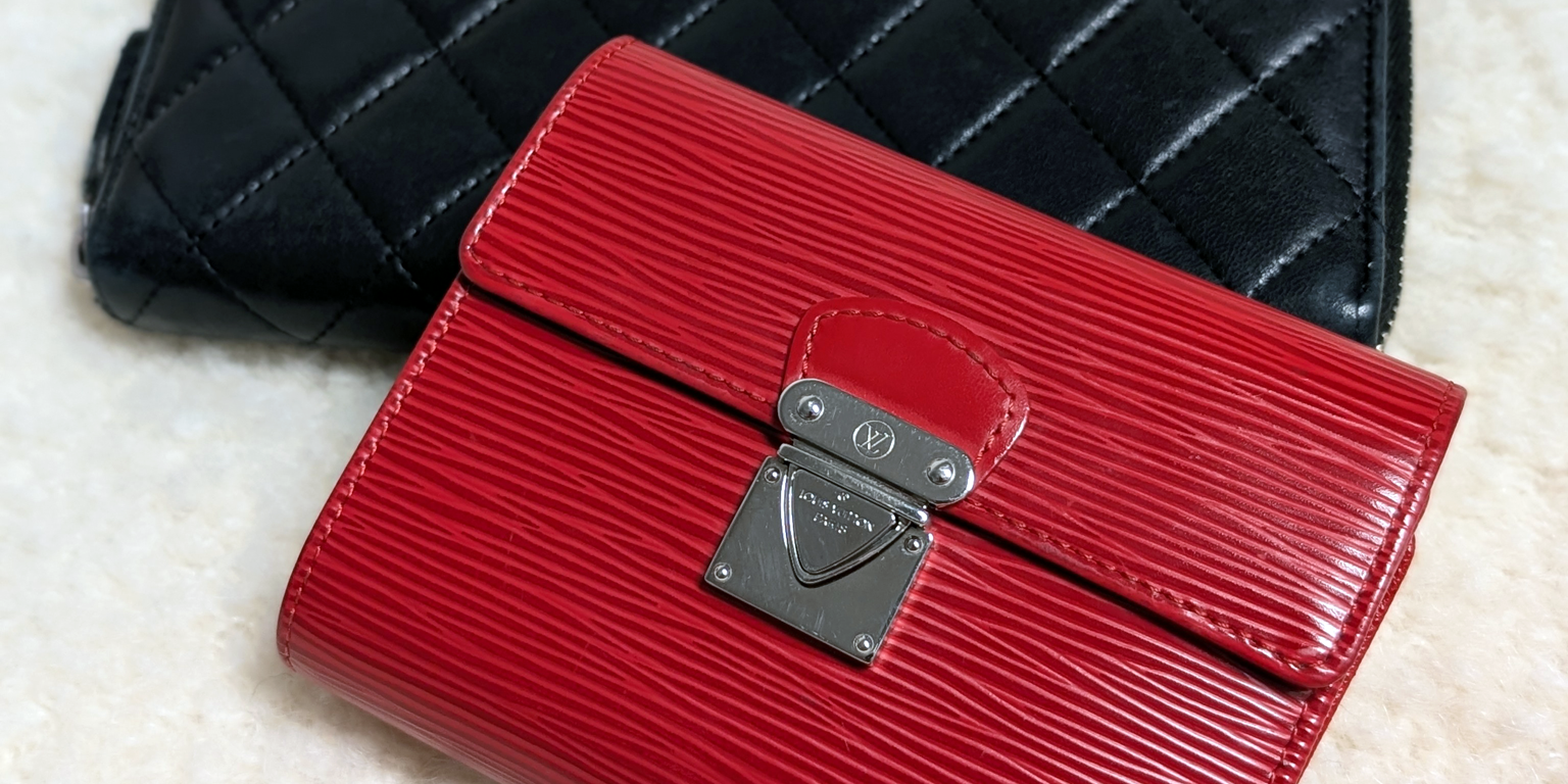Black quilted Chanel wallet and red Epi Leather Louis Vuitton wallet on a shearling cream background.