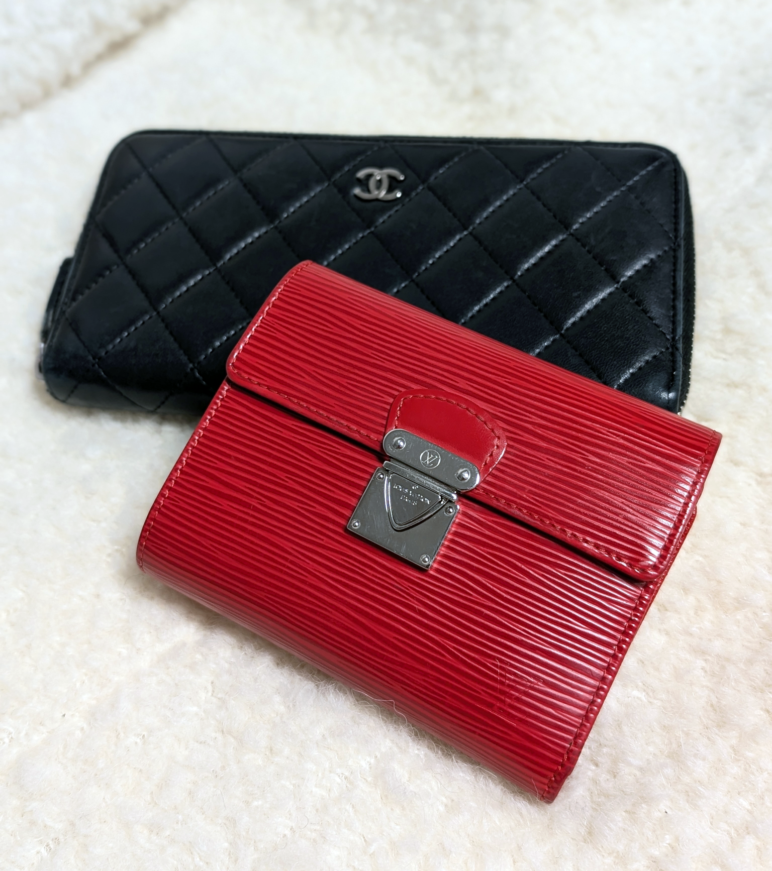 Black quilted Chanel wallet and red Epi Leather Louis Vuitton wallet on a shearling cream background.