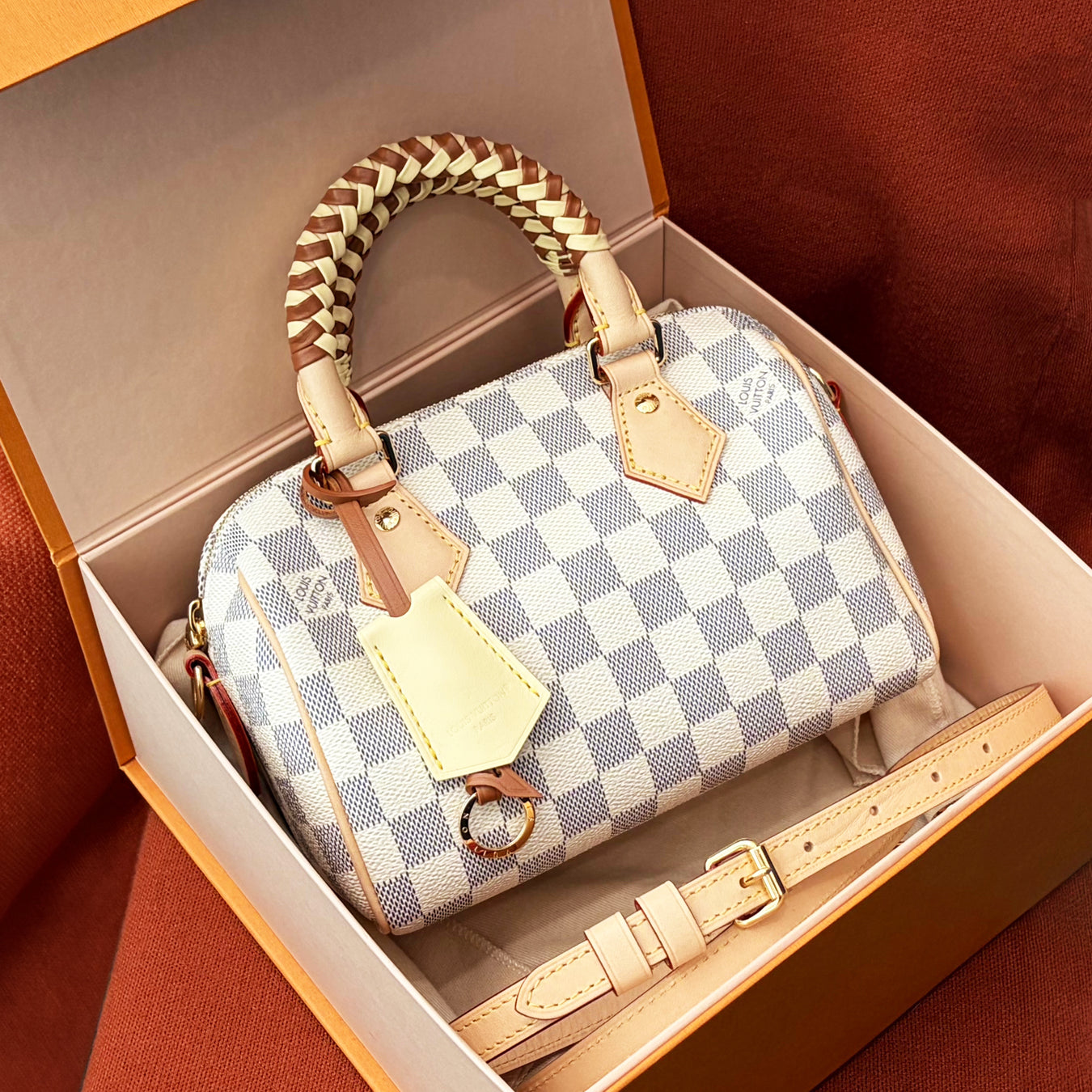Louis Vuitton Speedy 20 in Damier Azur in a box in front of an orange textile background.