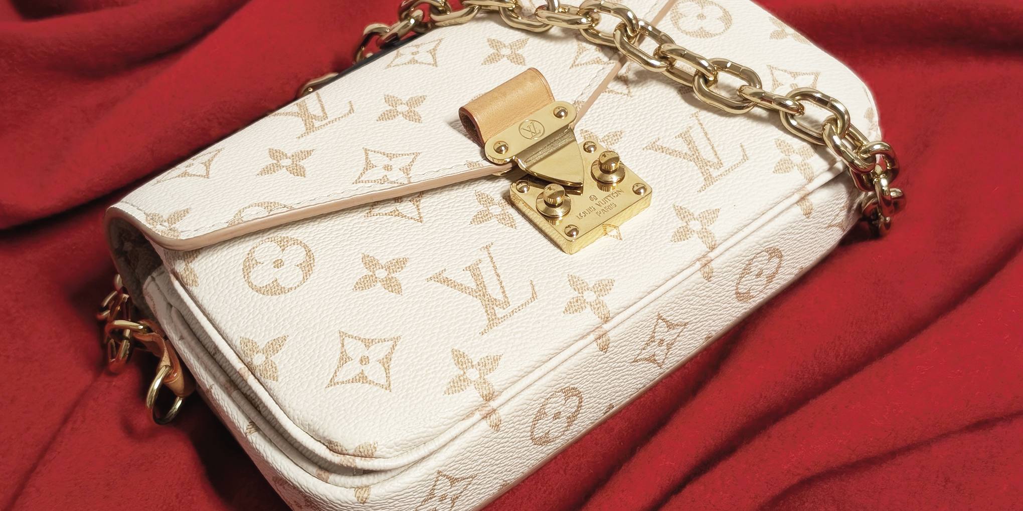 A Louis Vuitton Metis East/West Shoulder bag in beige against a red background.