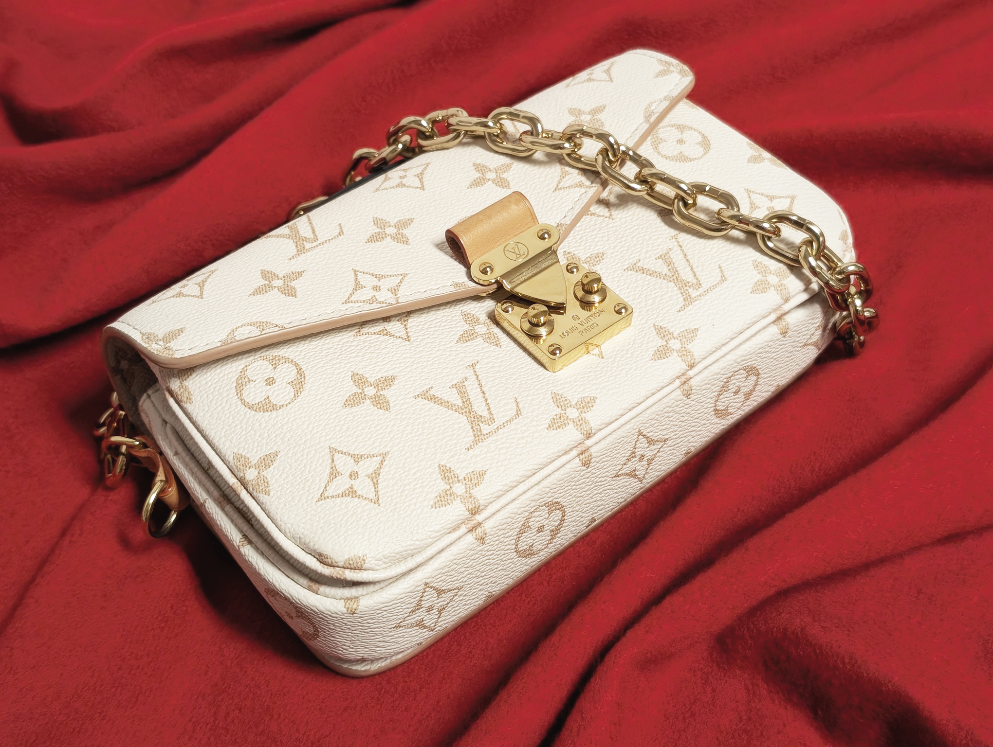 A Louis Vuitton Metis East/West Shoulder bag in beige against a red background.