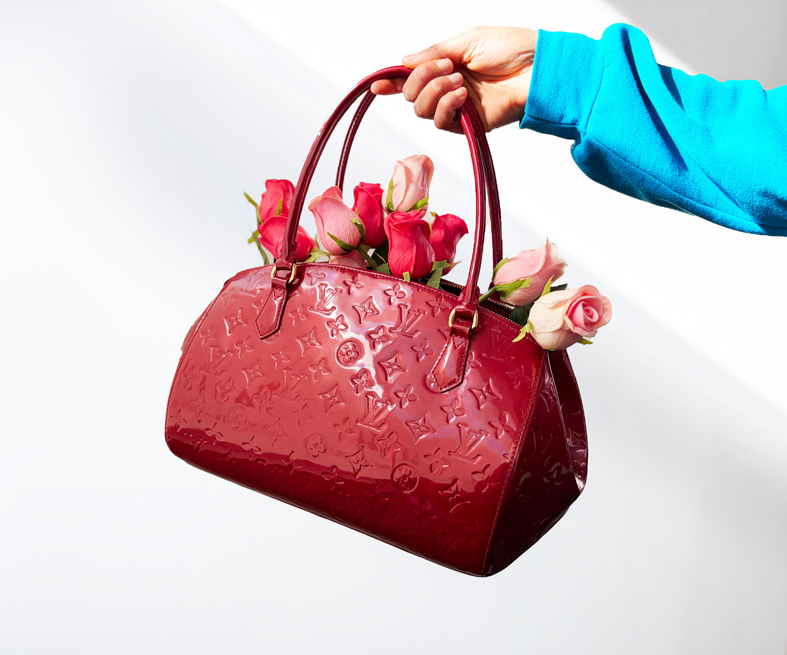 A Red Louis Vuitton empreinte leather handbag with pink and red roses inside, held by an arm covered by a blue hoodie sleeve.