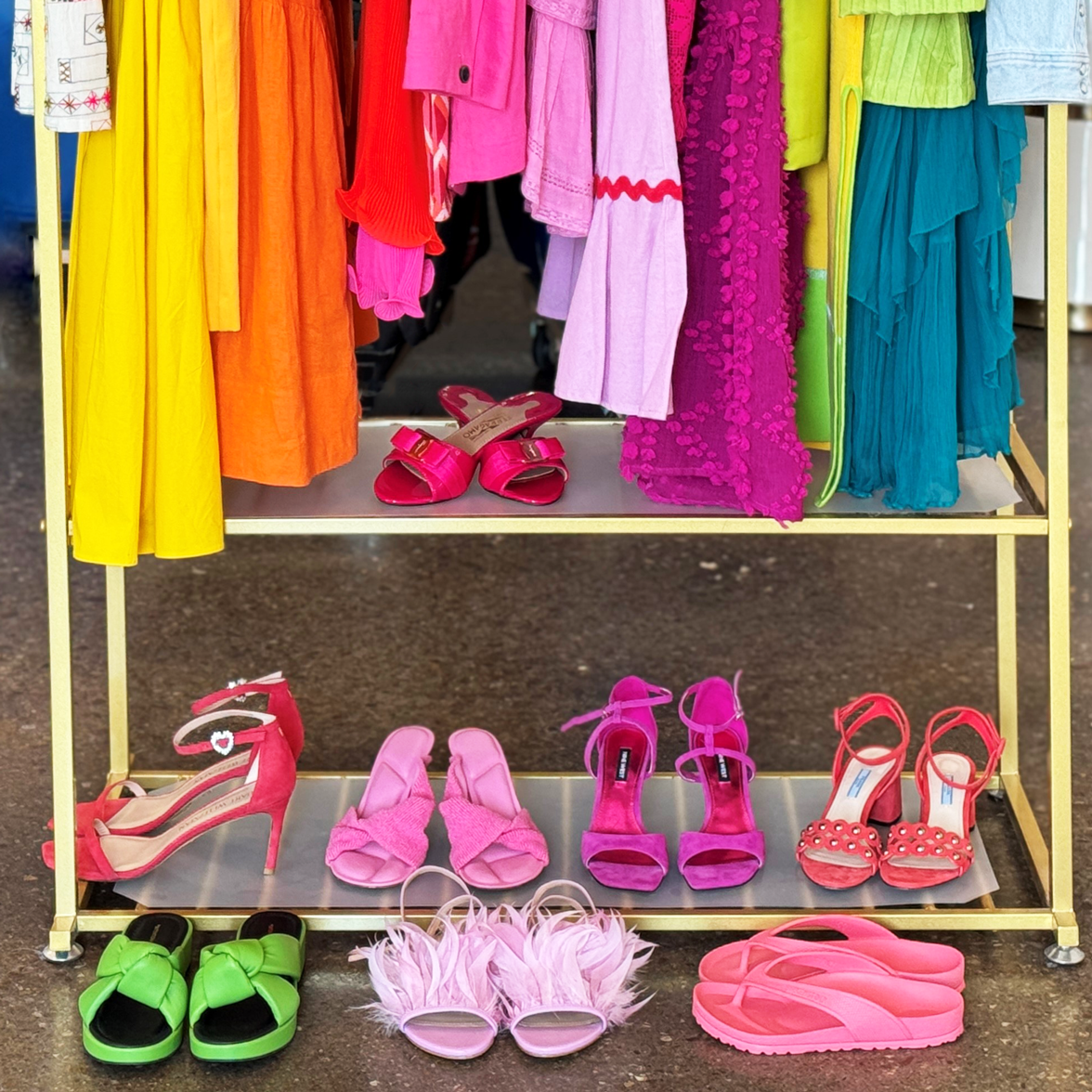 A photo of a variety of colorful designer clothing and shoe pieces on a gold rack.