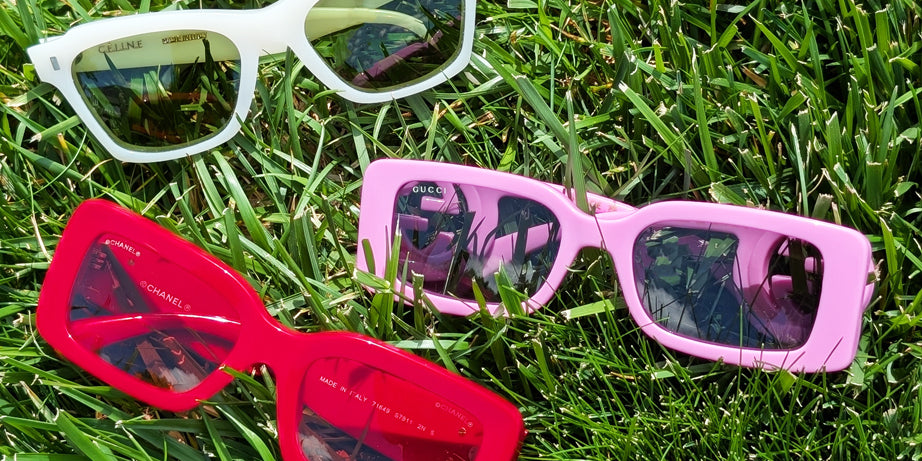 White, pink, and red designer sunglasses in grass on a sunny day.