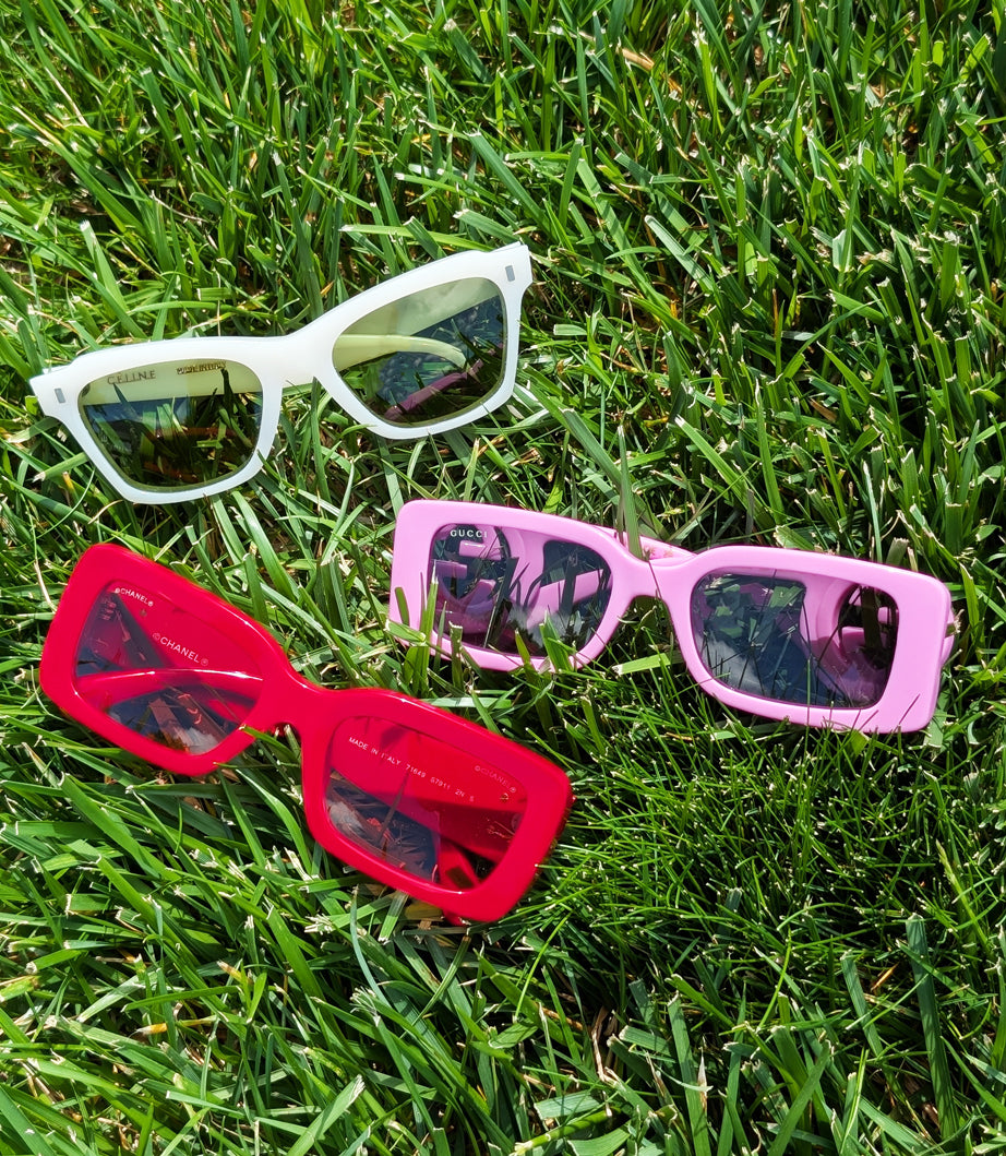 White, pink, and red designer sunglasses in grass on a sunny day.