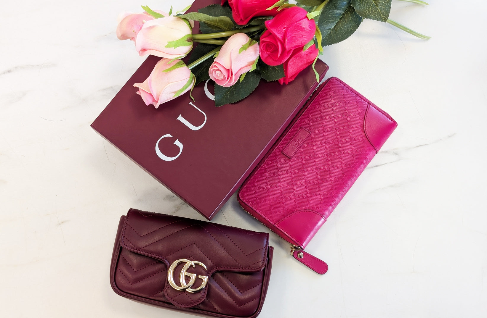 Gucci Handbag and wallet next to a red Gucci box with roses on top.