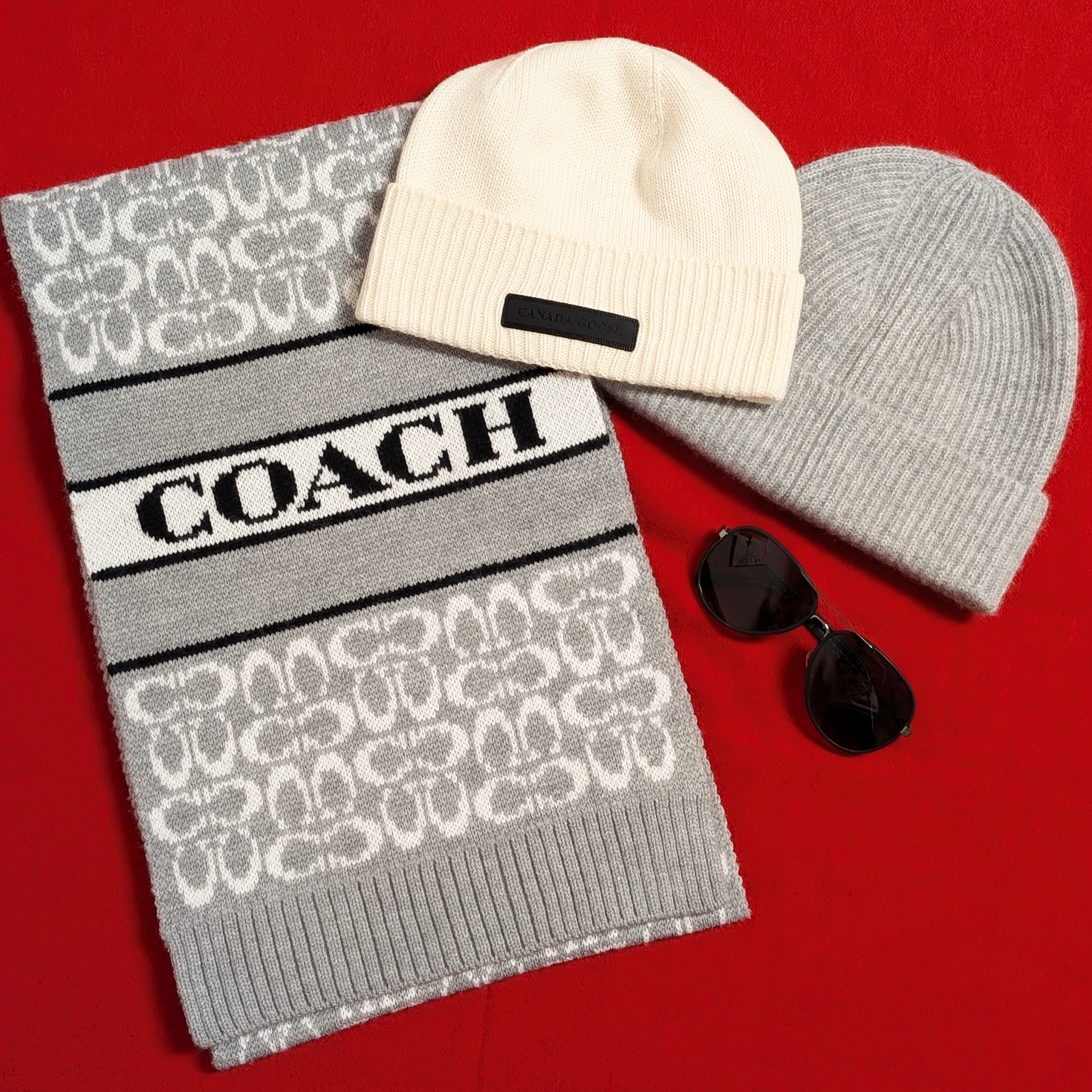 Gray coach scarf, a tan and a beige beanie, and a pair of sunglasses on a red background.