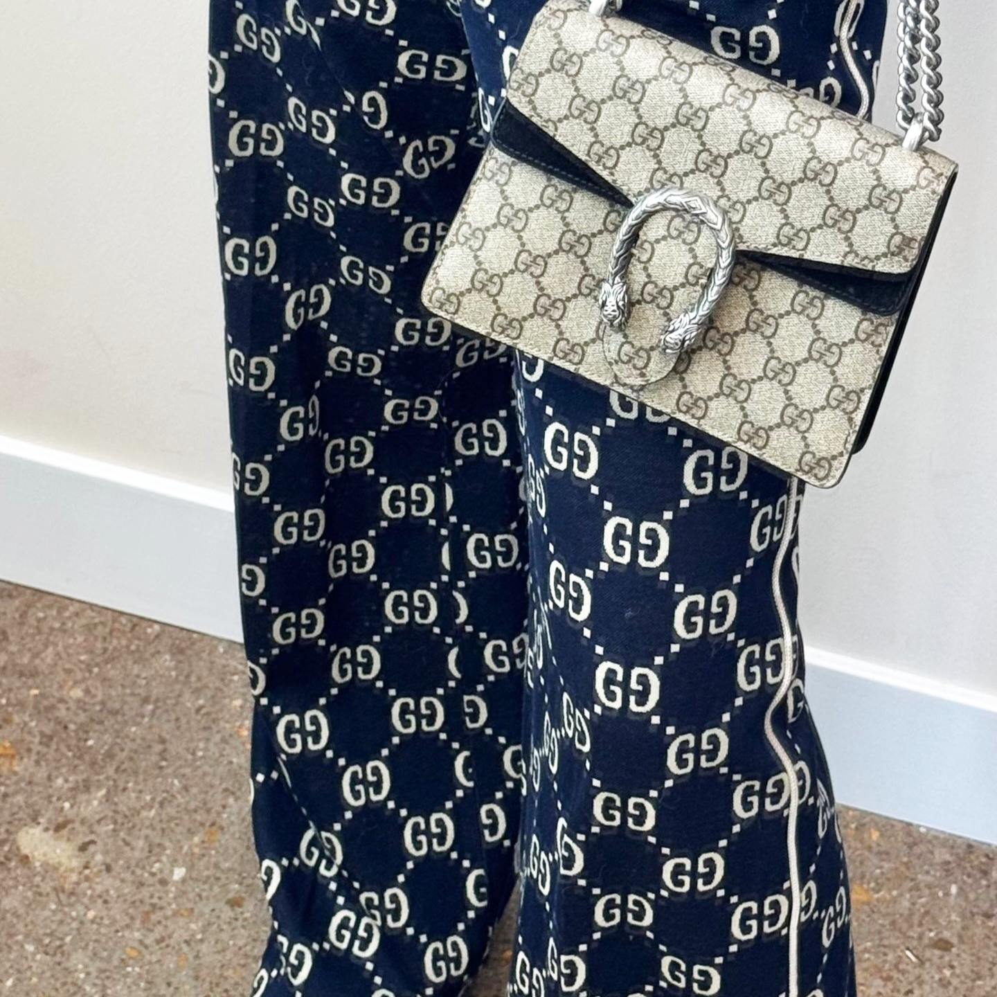 A woman wearing navy Gucci pants and holding a beige Gucci handbag.