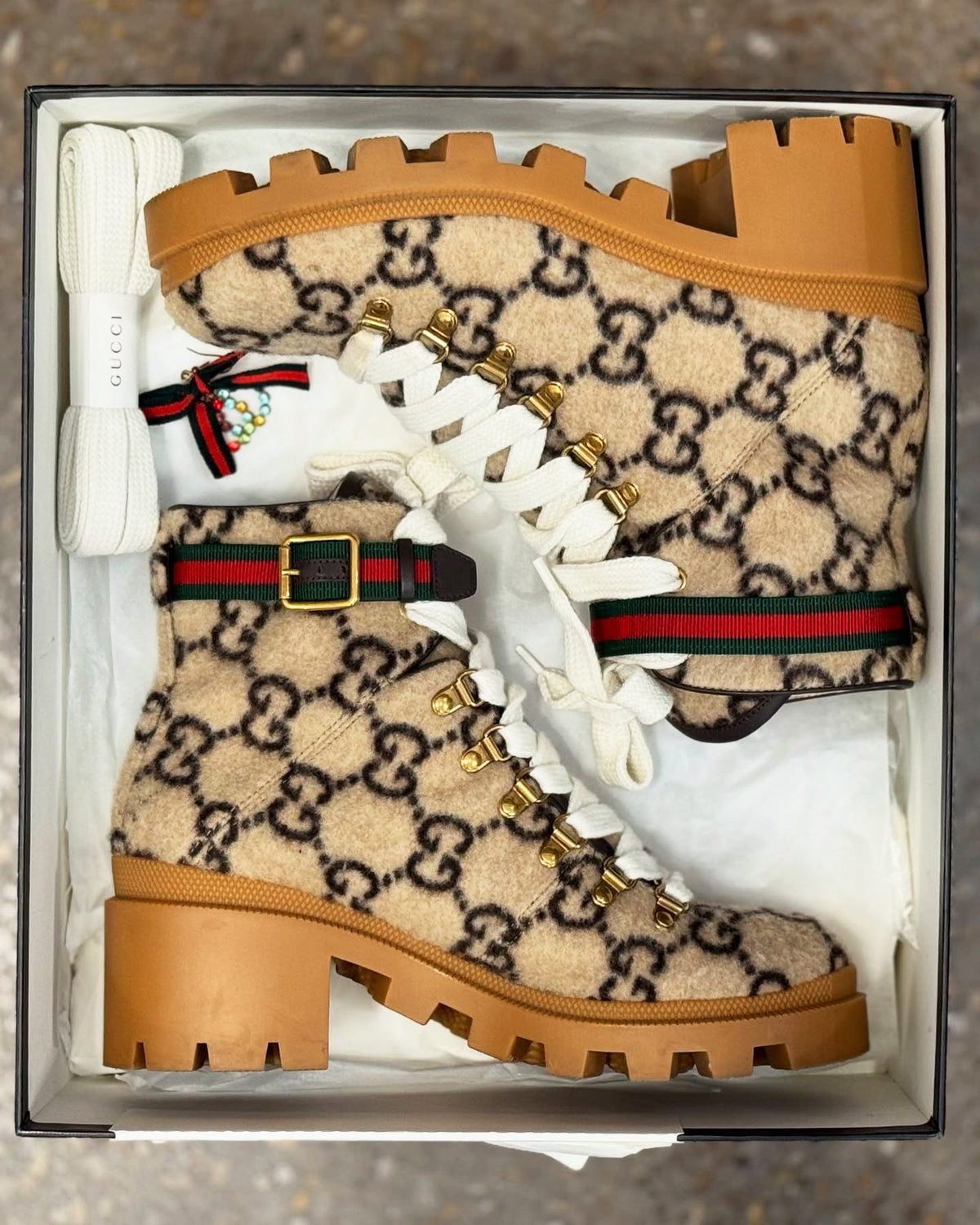 Beige Gucci boots with brown soles and white laces in a box.