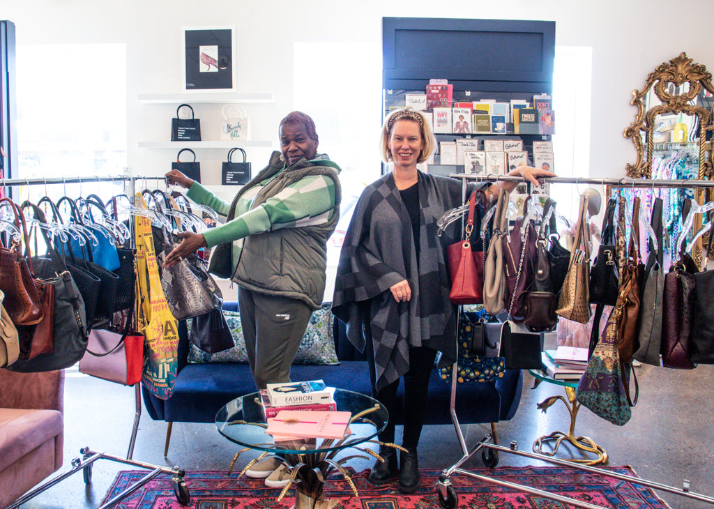 A photo of two women with racks full of handbags on either side.