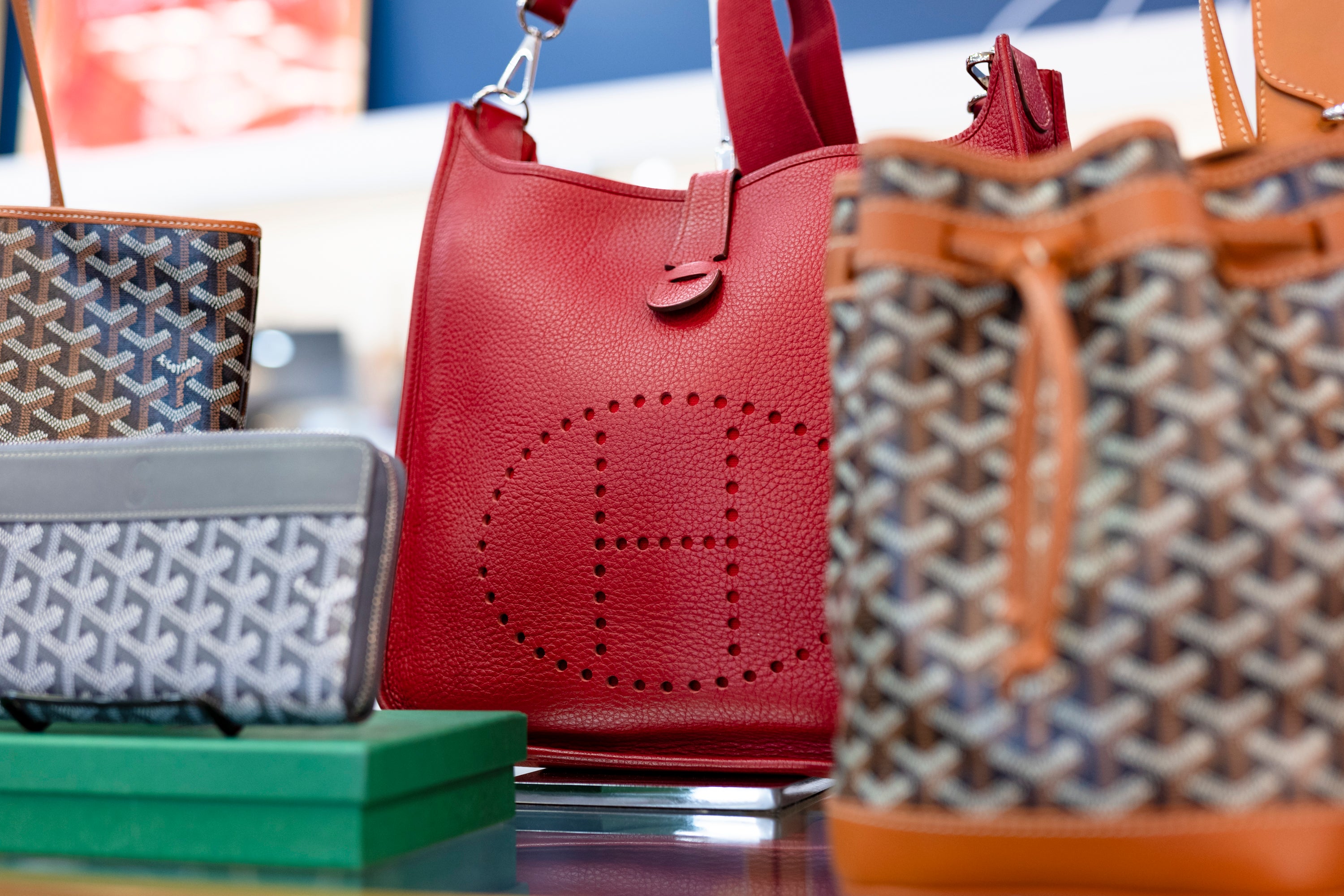 A photo of a red Hermes handbag surrounded by Goyard bags and a wallet.