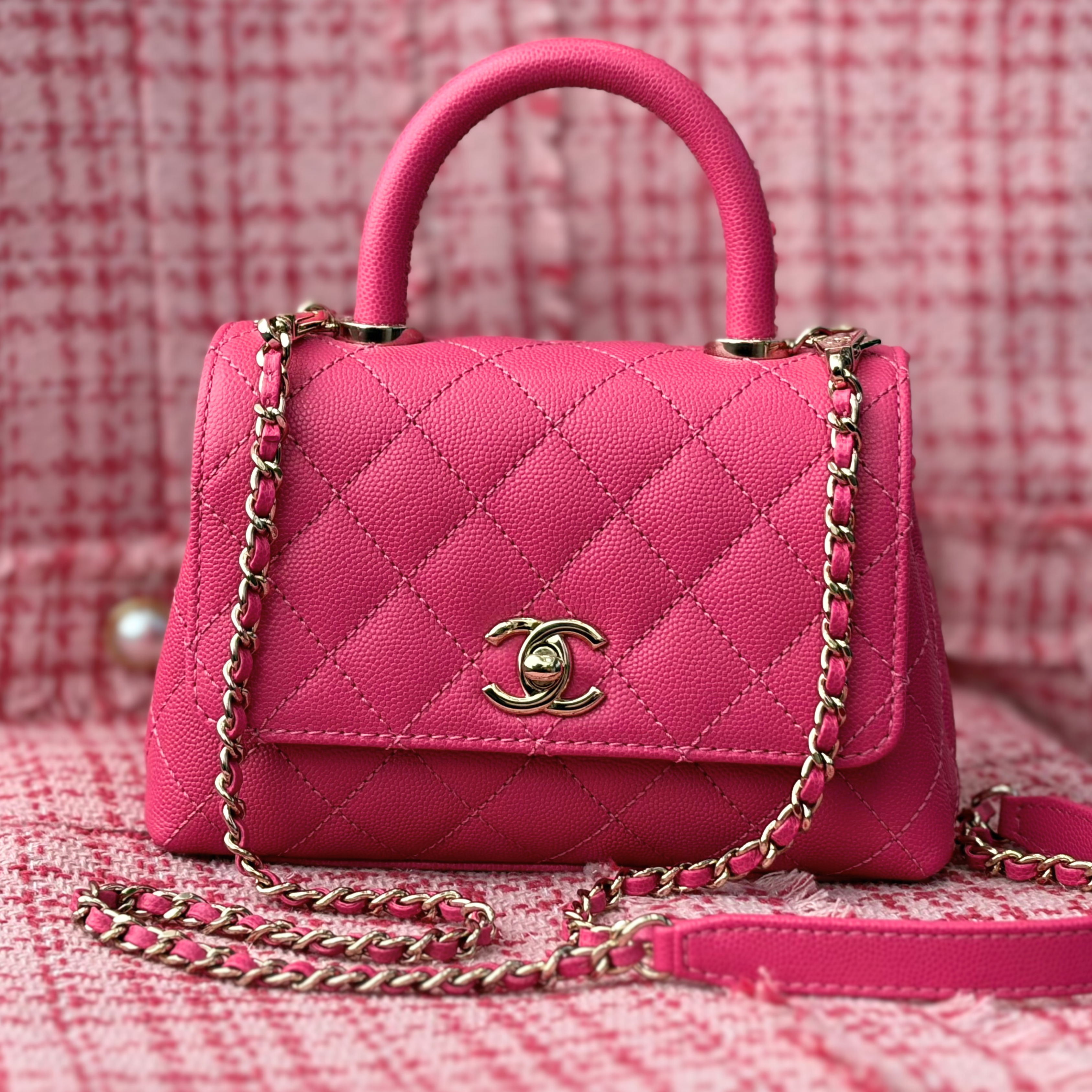 A pink Chanel handbag against a lighter pink tweed background.