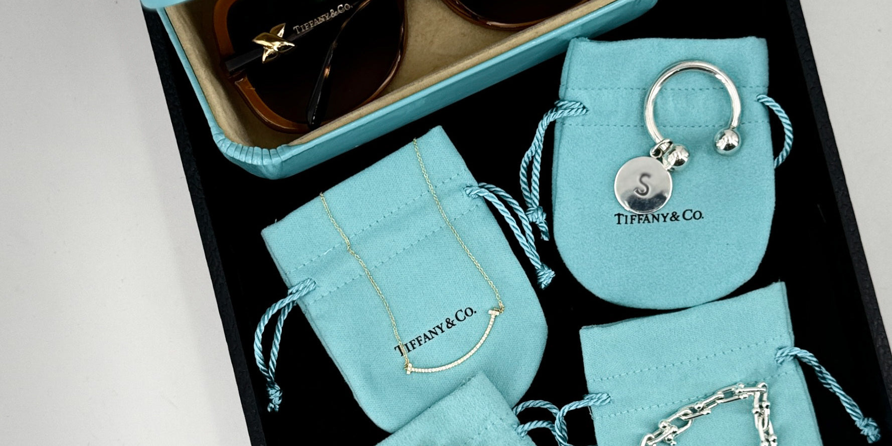 Tiffany & Co. jewelry set including sunglasses, keychain, and bracelets on branded pouches.