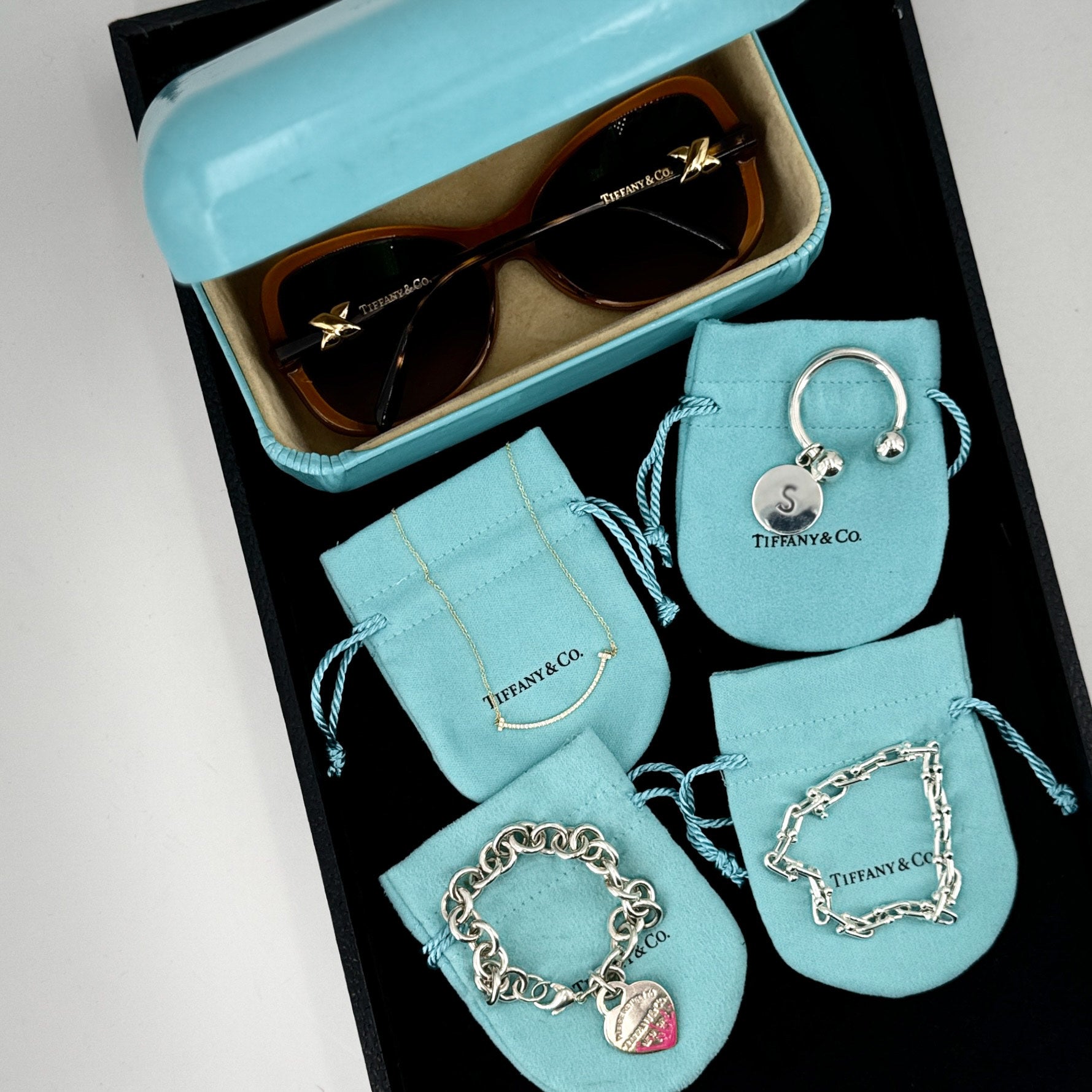 Tiffany & Co. jewelry set including sunglasses, keychain, and bracelets on branded pouches.